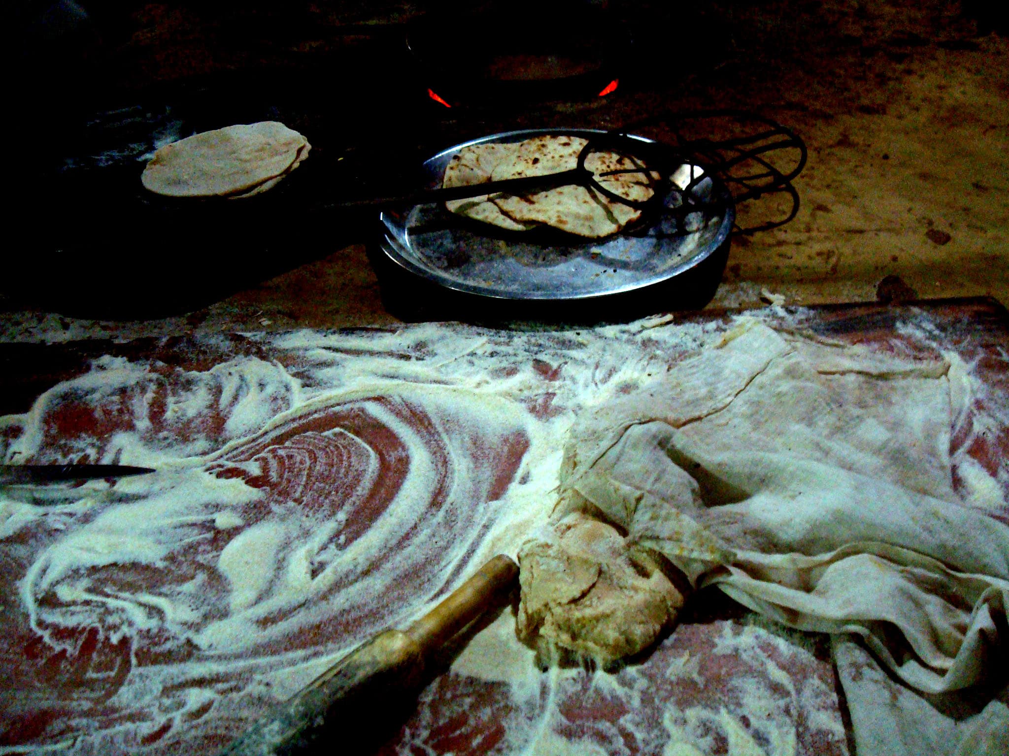 A flour-dusted roti-making surface at a dhaba — rolling pin, raw dough, and fresh rotis resting on a steel plate.